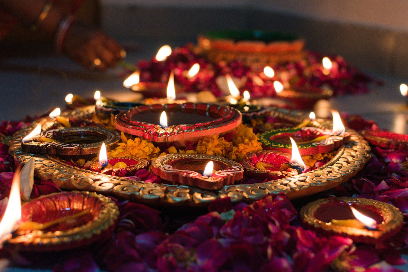 Lit clay oil lamps on a decorative tray surrounded by flower petals