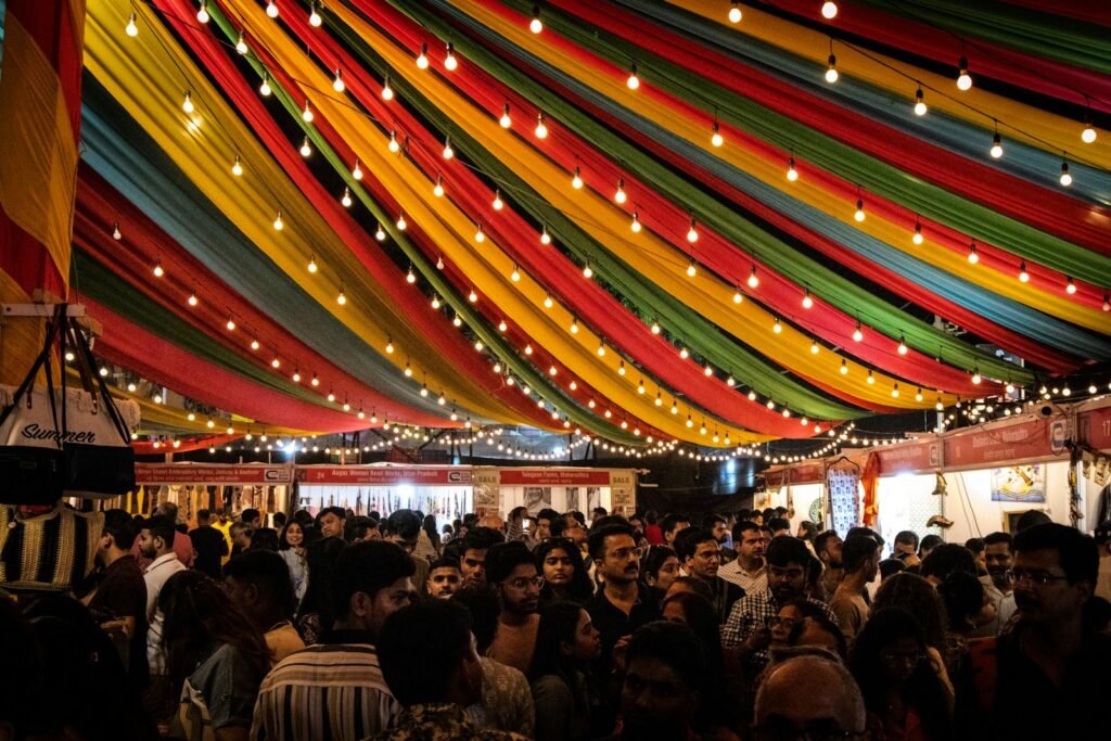 Crowd gathered under colorful draped fabric and string lights at a festival