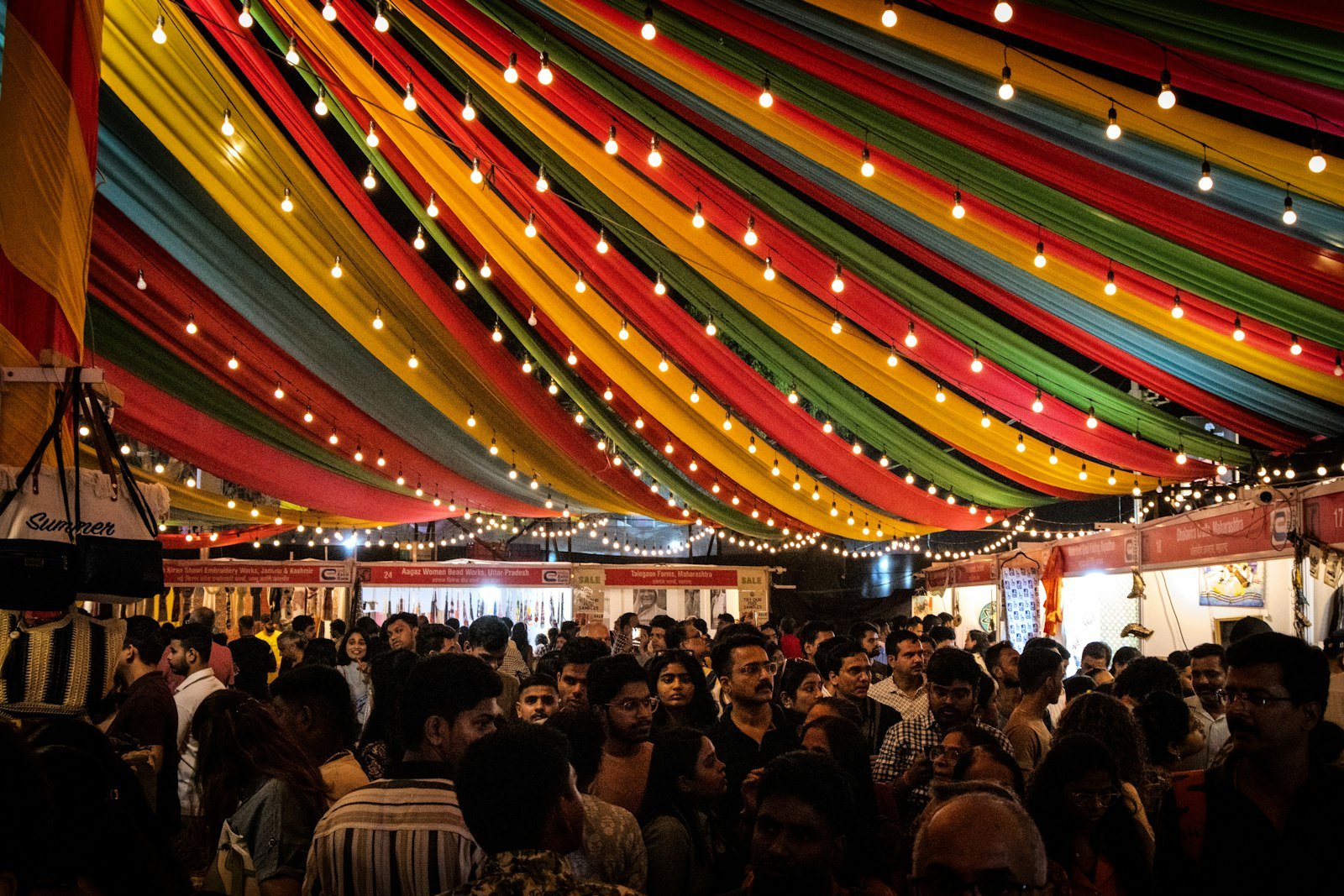 Crowd gathered under colorful draped fabric and string lights at a festival