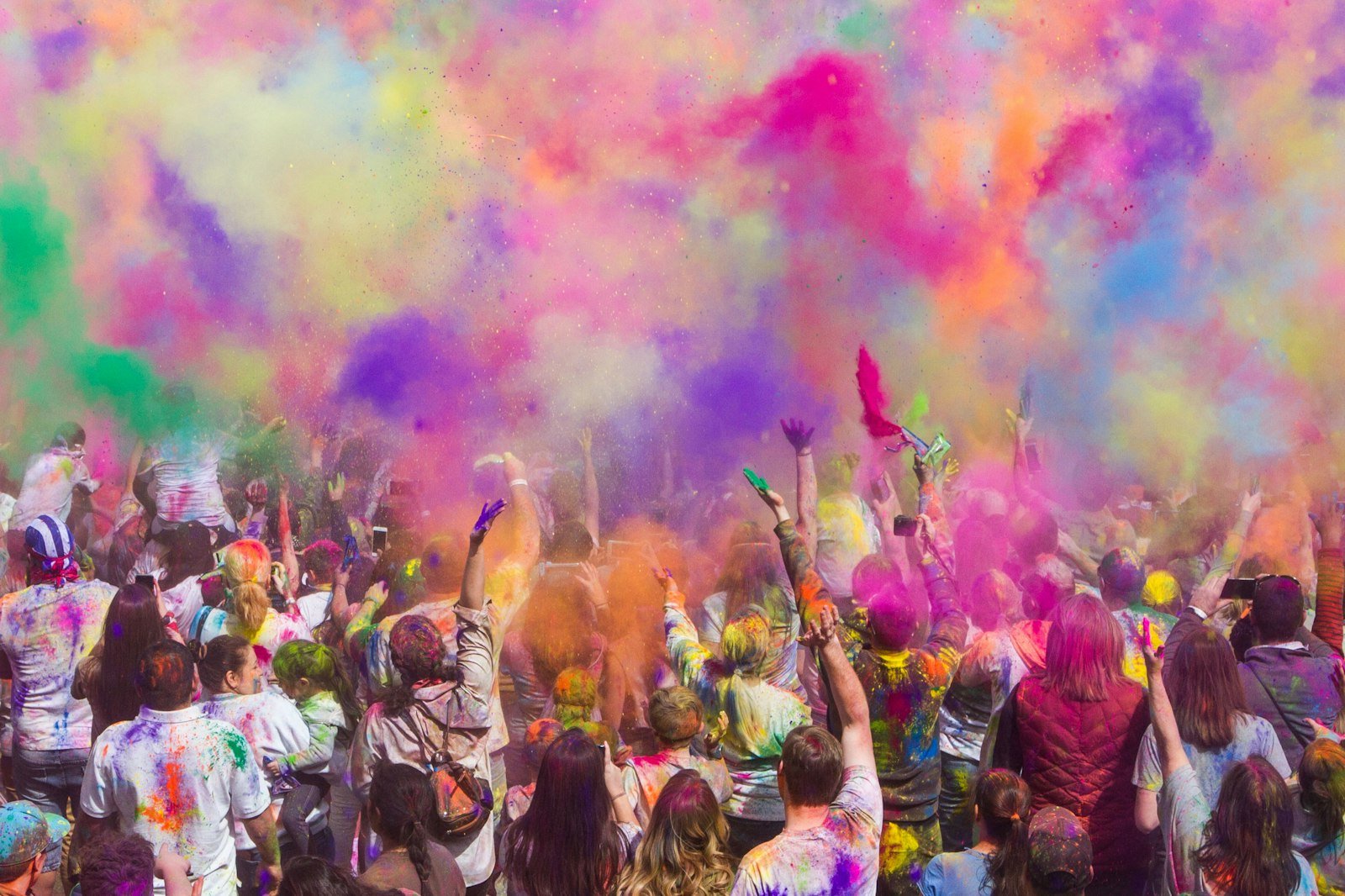A crowd of people throwing colorful powder into the air during Holi festival
